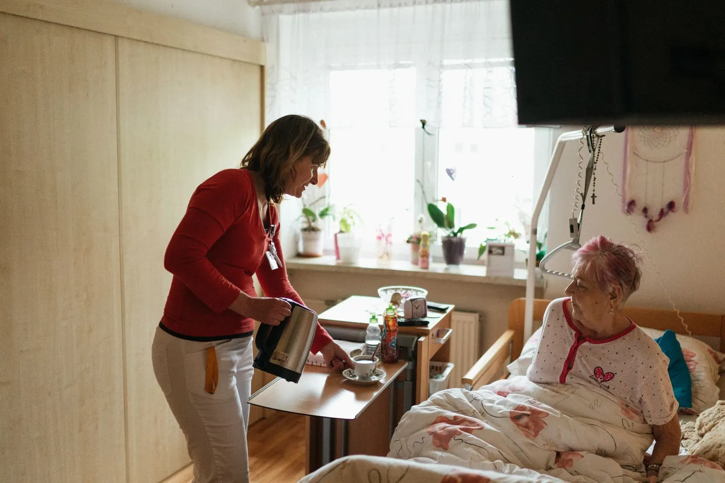 Pflegerin bringt einer älteren Frau im Bett eine Tasse Tee