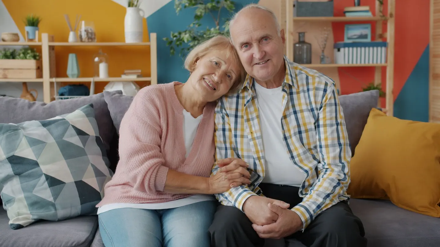 Älteres Paar sitzt entspannt und lachend auf dem Sofa