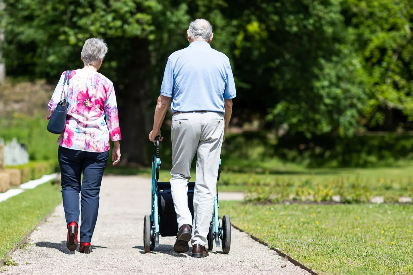 Älteres Paar geht mit Rollator einen Parkweg entlang